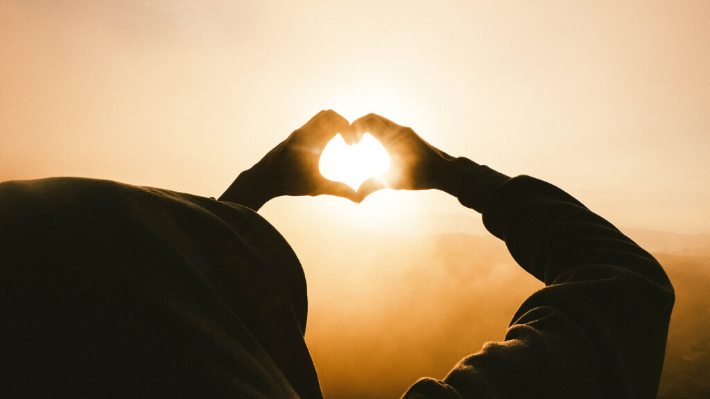 Mann formt Hände zu Herz und Sonnenstrahlen strahlen durch